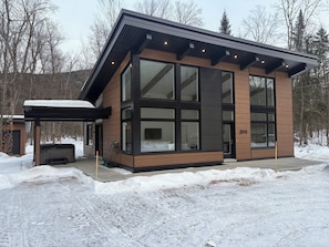 A modern two-story building with large windows and a wooden facade, surrounded by snow. - Luxury nature chalet | Modern | Spa (St-Raymond)