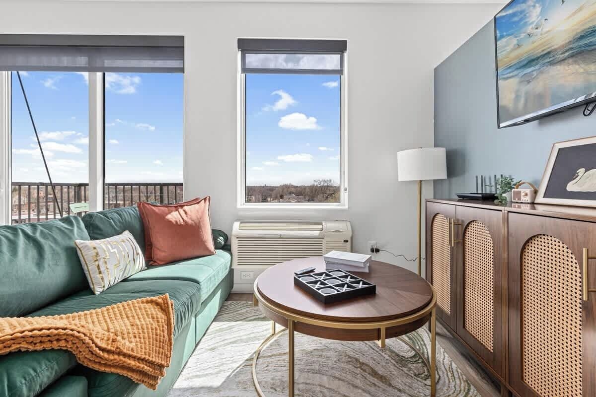 A modern living room with a green sofa, a round coffee table, and a view of the outdoors through large windows.