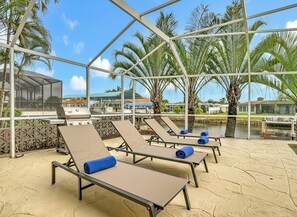 A covered outdoor lounge area with sun loungers, a grill, and palm trees. - Heated Saltwater Pool, 3 Bed, 2 Bath Joyful Waterside (Cape Coral)