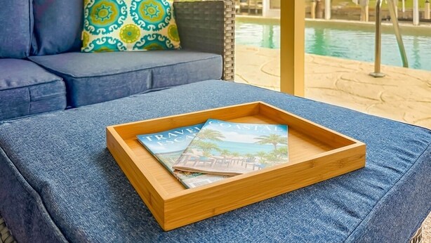 Ein hölzerner Tablett mit Zeitschriften auf einer blauen, gepolsterten Sitzbank am Pool.