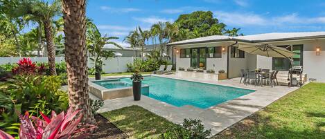 A modern house with a swimming pool, patio furniture, and lush greenery.