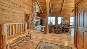 A log cabin interior with a stone fireplace, wooden flooring, a bench, and a sofa. -  Acorn Abbey - Lakeside Retreat w/3BRs, spring on the water! (Murphy)