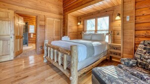 A wooden cabin bedroom with a bed, a chair, and a window. -  Acorn Abbey - Lakeside Retreat w/3BRs, spring on the water! (Murphy)