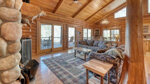 A log cabin interior with a stone wall, wooden ceiling, a large sofa, a coffee table, and a fireplace. -  Acorn Abbey - Lakeside Retreat w/3BRs, spring on the water! (Murphy)
