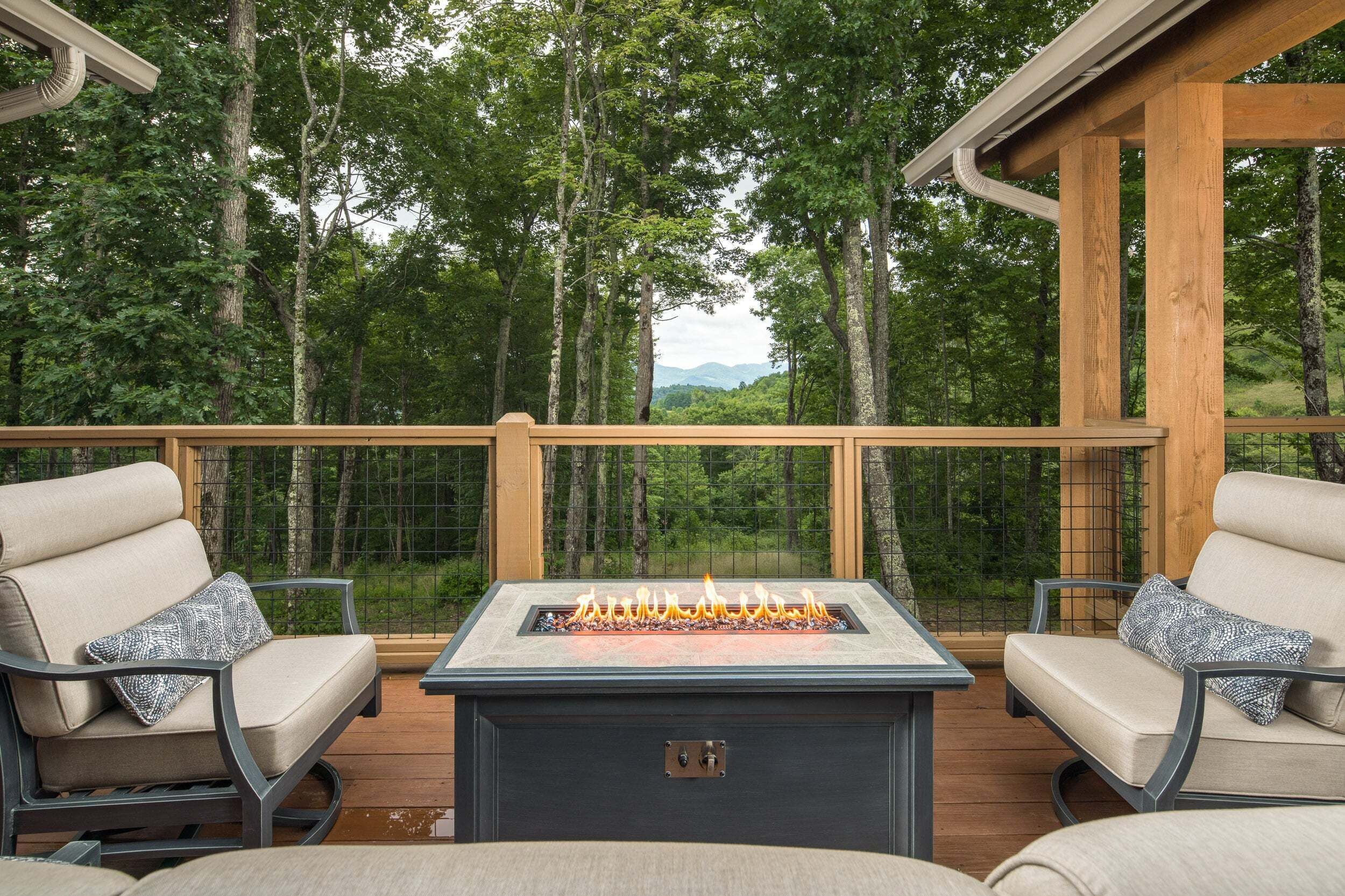 A deck with a fire pit, two chairs, and a view of a forest.
