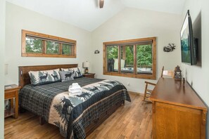 A bedroom with a large bed, two nightstands, a wooden dresser, and two windows with views of greenery. - Luxury 4 BR Mountain Escape: Views, Hot Tub & Pool Table (Banner Elk)