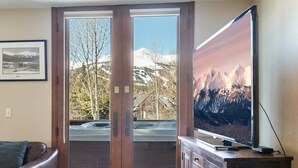 Una sala de estar con puerta de cristal corredera que da a un balcón, televisor de pantalla plana montado en la pared y sofá de cuero marrón.