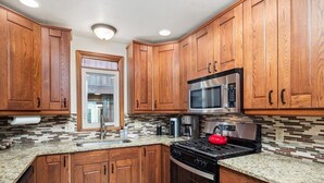 Una cocina con armarios de madera, encimeras de granito, un microondas de acero inoxidable, un hervidor rojo y un horno empotrado.