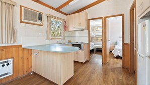 A compact kitchen with wooden cabinets, a built-in stove, and a window with curtains. - Tiny Away Stay – Laanecoorie Lakeside (Laanecoorie)