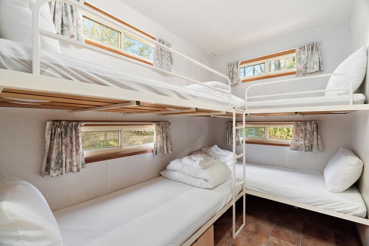 A bunk bed room with two windows, curtains, and a tiled floor.