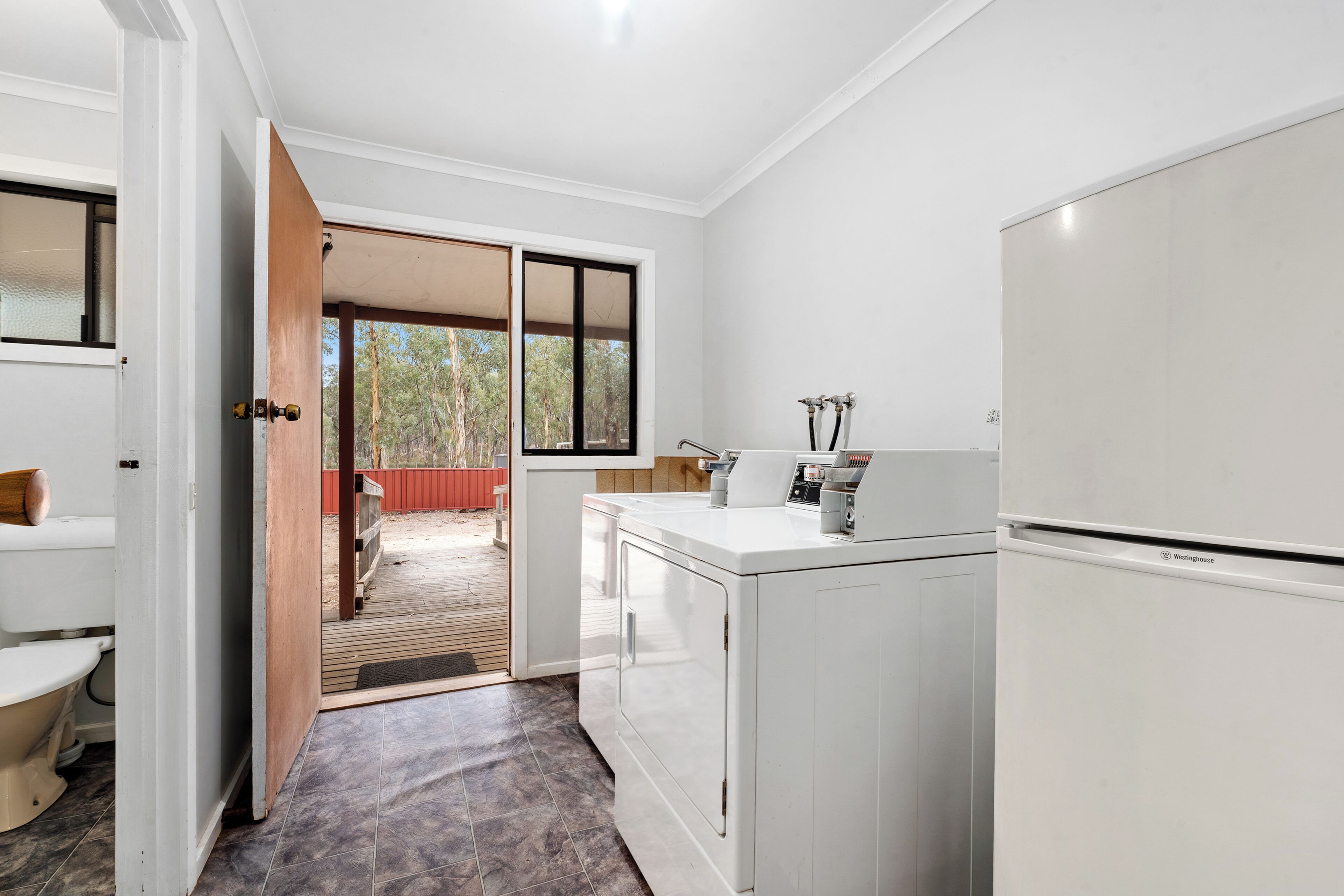 Una cocina moderna con lavadora y secadora integradas, una puerta de madera que da a un balcón y vistas a árboles.
