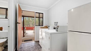 Una cocina moderna con lavadora y secadora integradas, una puerta de madera que da a un balcón y vistas a árboles.