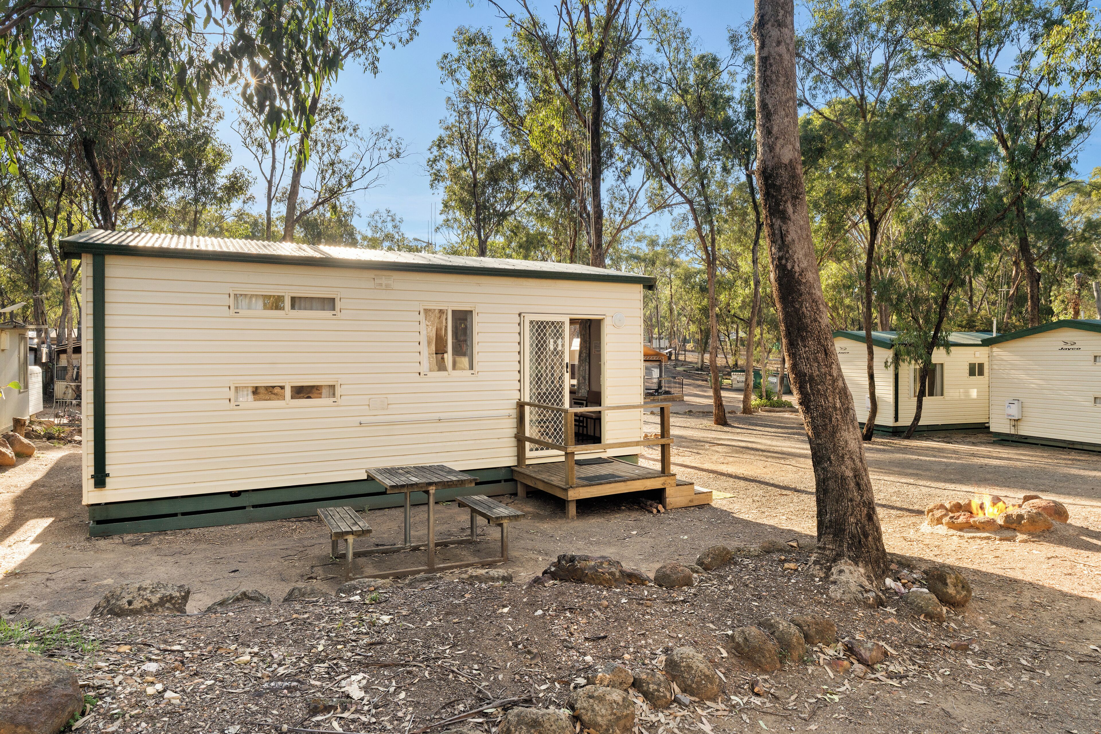 A single-story mobile home with a porch, a small table, and a bench.