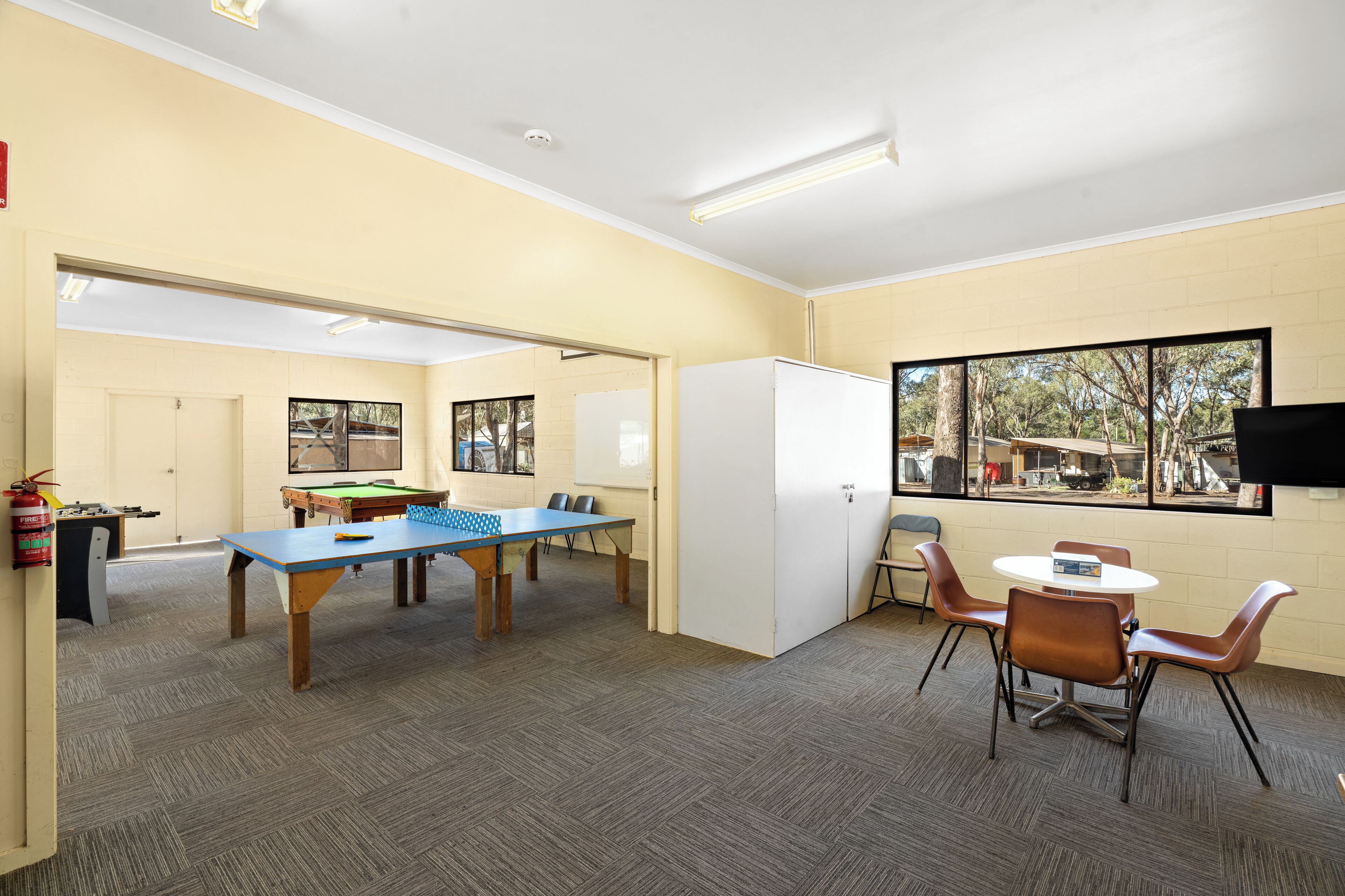 A room with a pool table, a ping pong table, and a billiards table. There are chairs and a small table with a whiteboard.