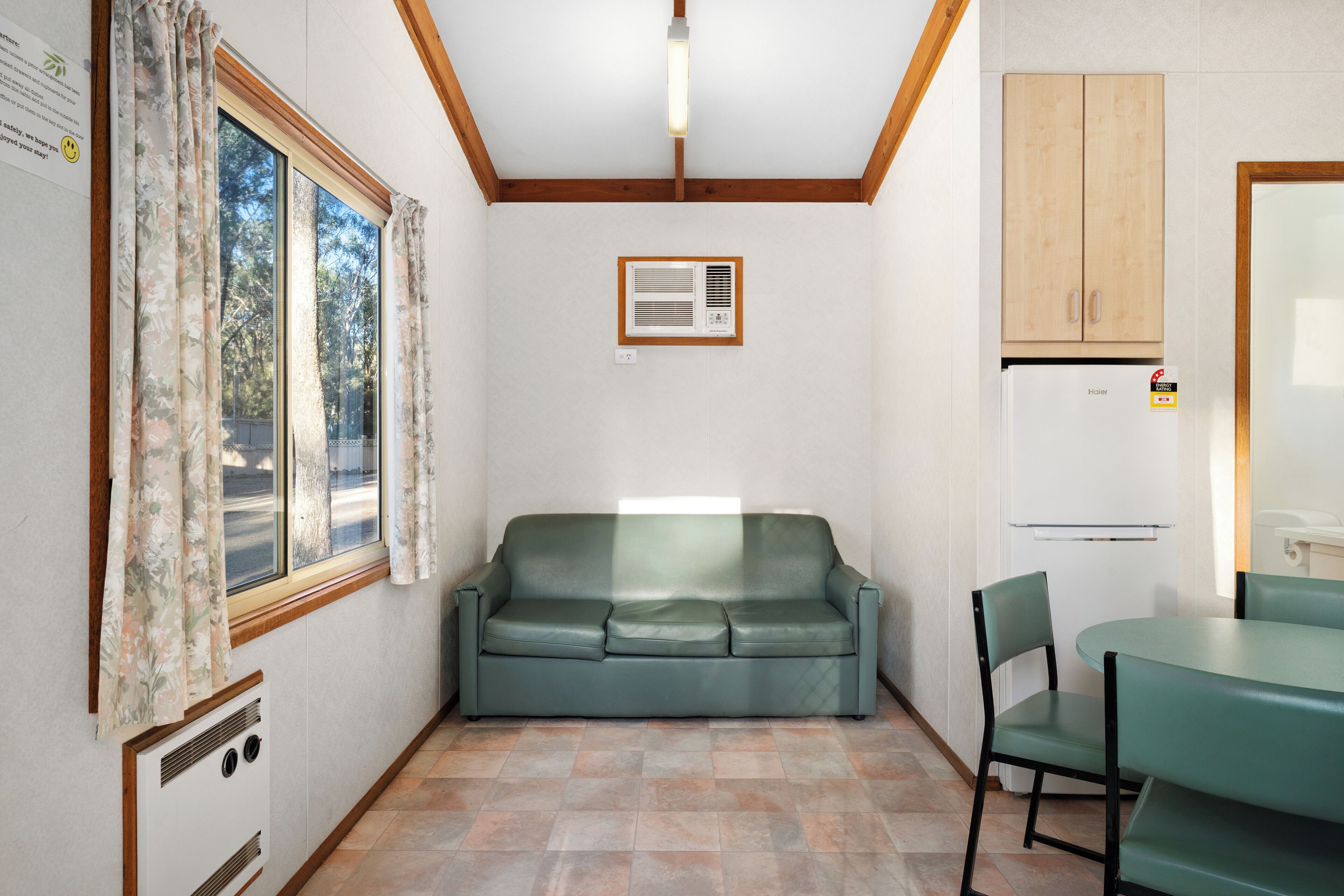 A compact kitchen with a built-in refrigerator, a window with curtains, a sofa, and a dining table with chairs.
