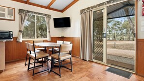 A dining area with a table and chairs, a television on the wall, and a sliding glass door leading to an outdoor area. - Tiny Away Stay – Laanecoorie Lakeside (Laanecoorie)