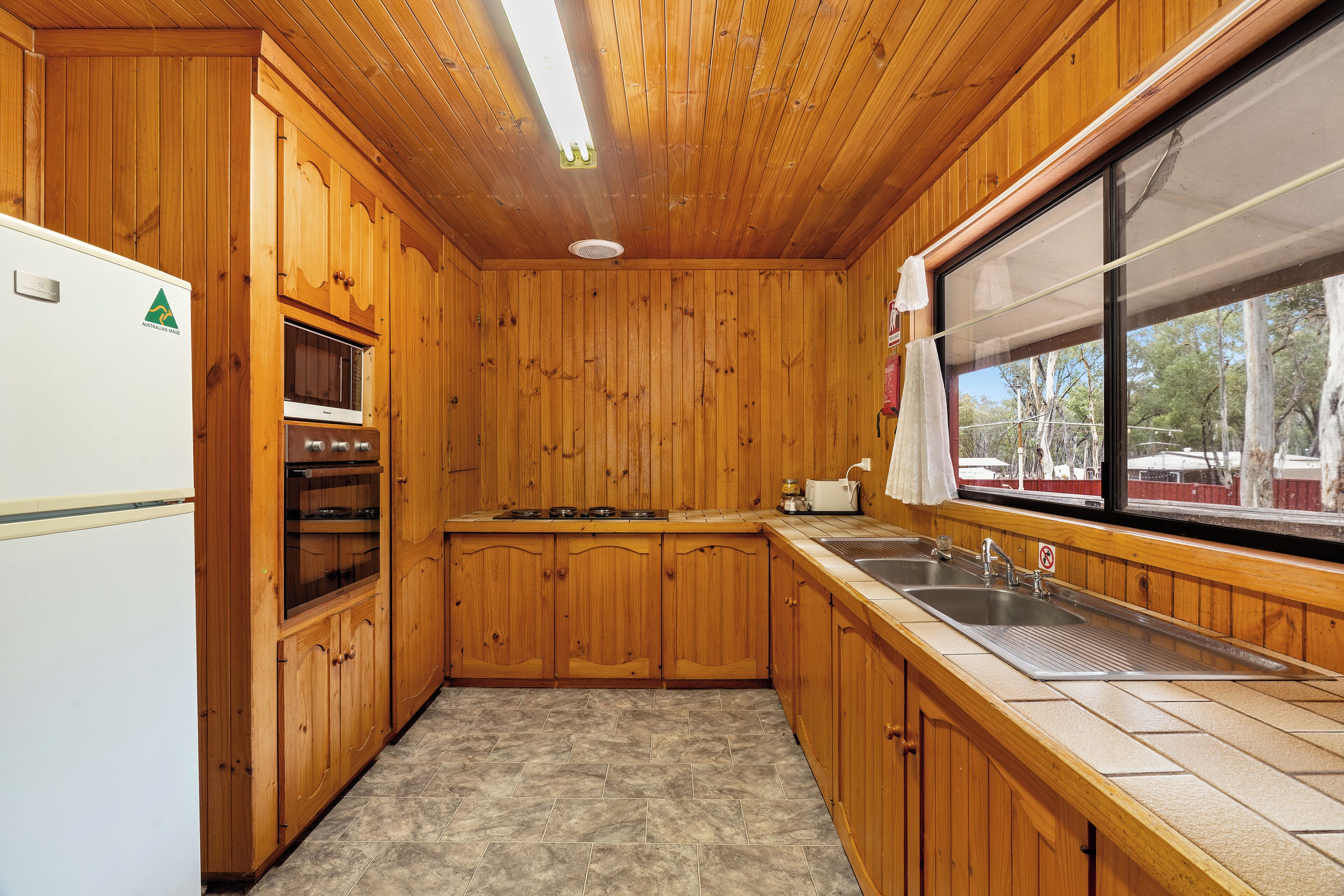 Eine Küche mit Holzwänden, einem Kühlschrank, einem Backofen, einem Herd und einem Waschbecken.