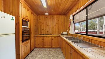 Eine Küche mit Holzwänden, einem Kühlschrank, einem Backofen, einem Herd und einem Waschbecken.