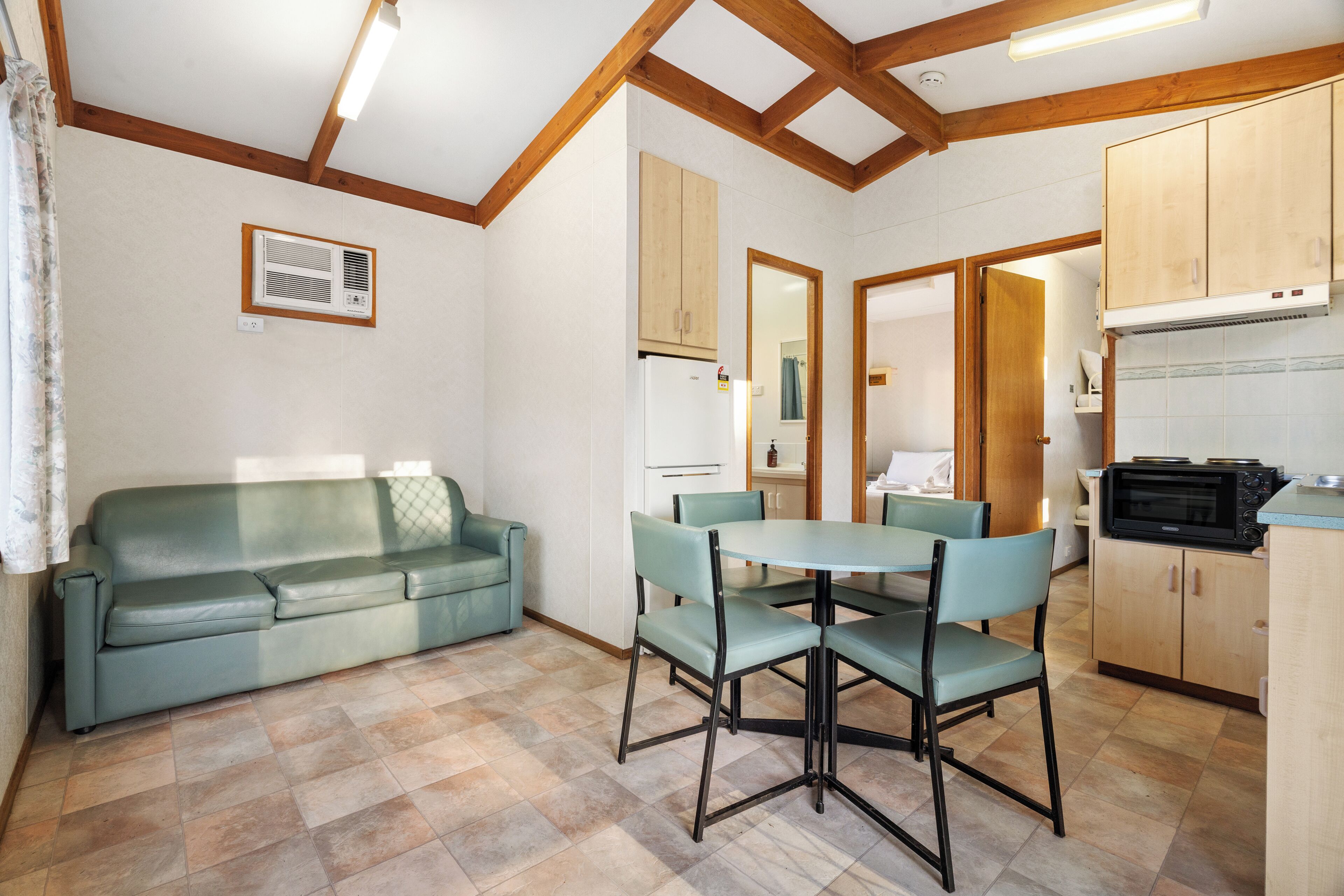 A room with a sofa, dining table, chairs, wooden cabinets, and a microwave.