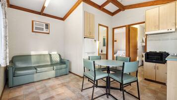 A room with a sofa, dining table, chairs, wooden cabinets, and a microwave.