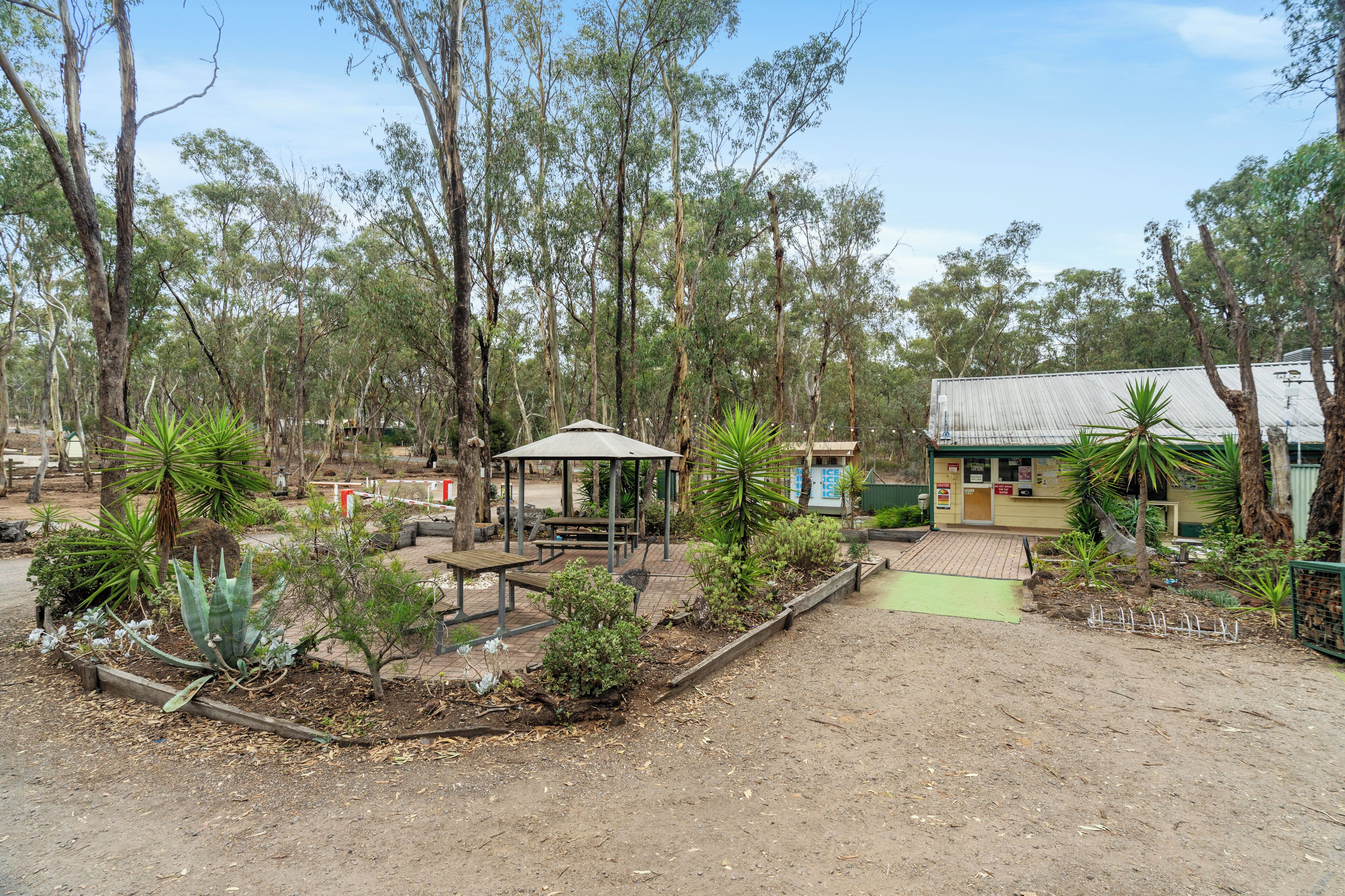 A park with a gazebo, picnic tables, and a building with a corrugated metal roof.