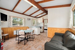 Ein Zimmer mit Holzboden, einem Esstisch mit Stühlen, einer Couch und einer Küchenzeile mit Schränken und Herd.