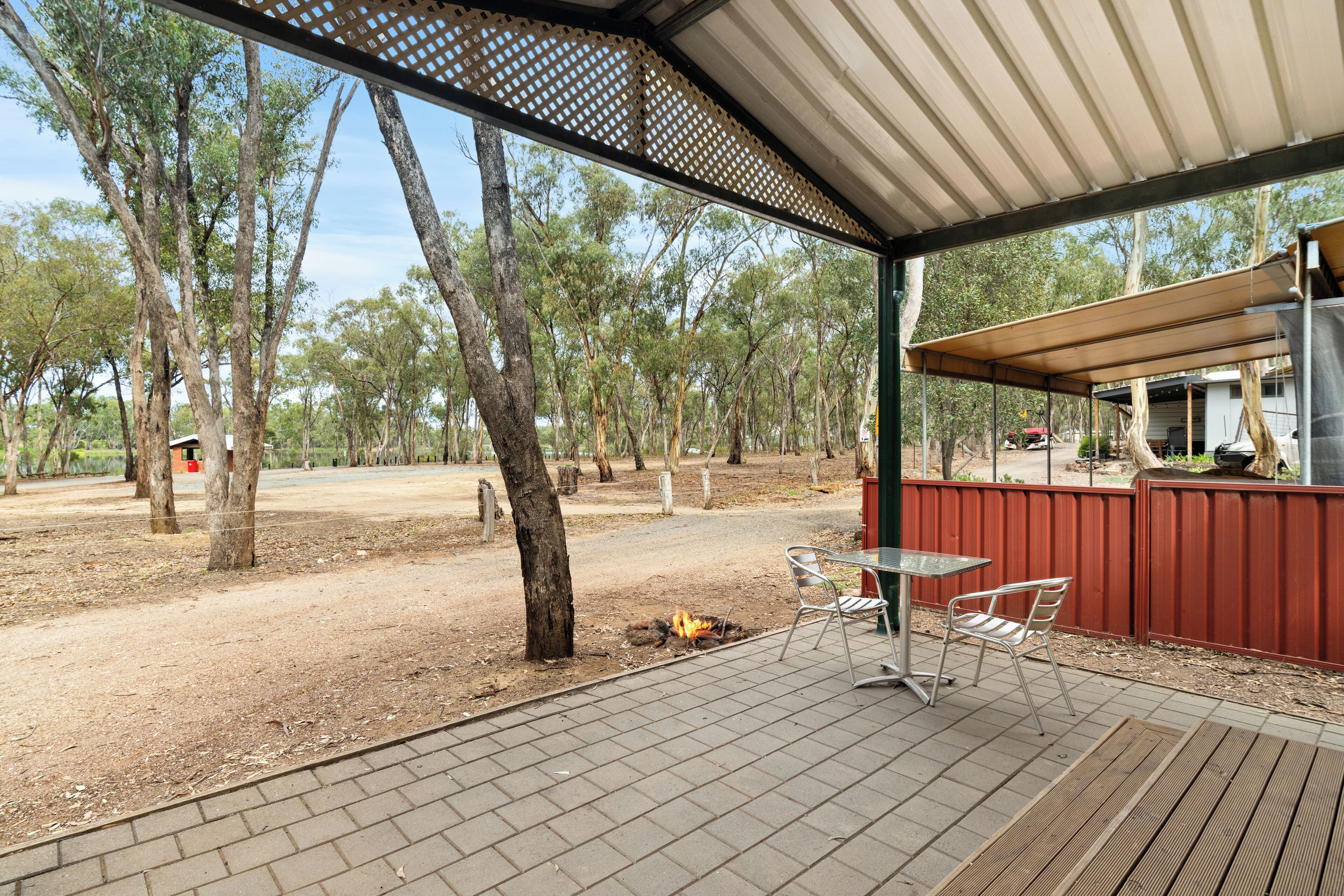 An outdoor patio with a table and chairs, surrounded by trees and a barbecue area.