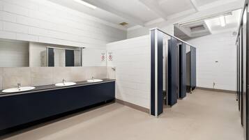 Un baño público con paredes de azulejos blancos, una larga barra con lavamanos y un espejo.