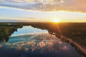 A serene landscape with a lake reflecting the sky, surrounded by dense forest and a distant shoreline. - Tiny Away Stay – Laanecoorie Lakeside (Laanecoorie)