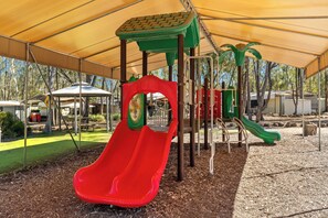 Ein Spielplatz mit einer roten Rutsche, grünen Klettergerüsten und einem überdachten Bereich.