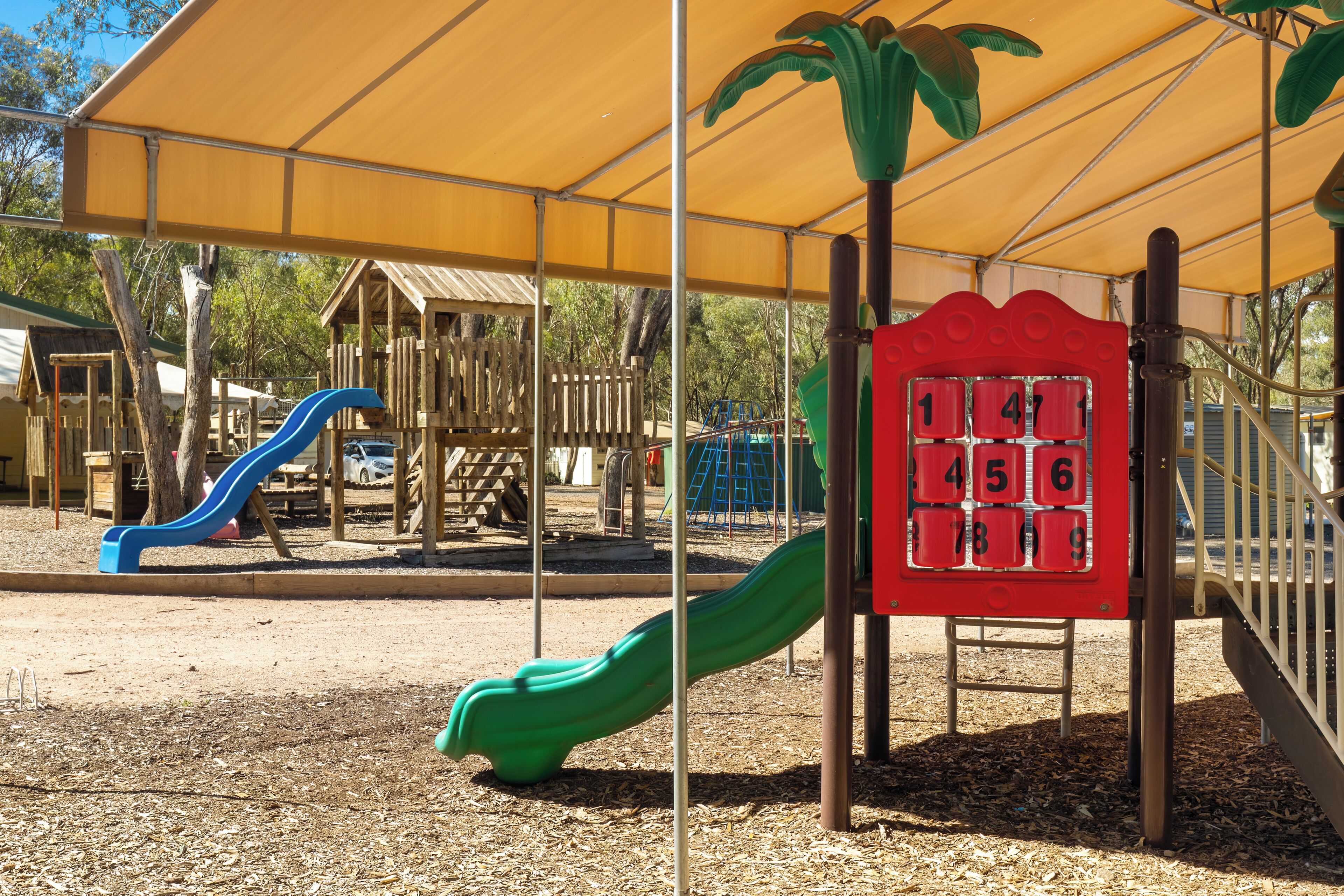 A playground with slides and a climbing structure under a canopy.
