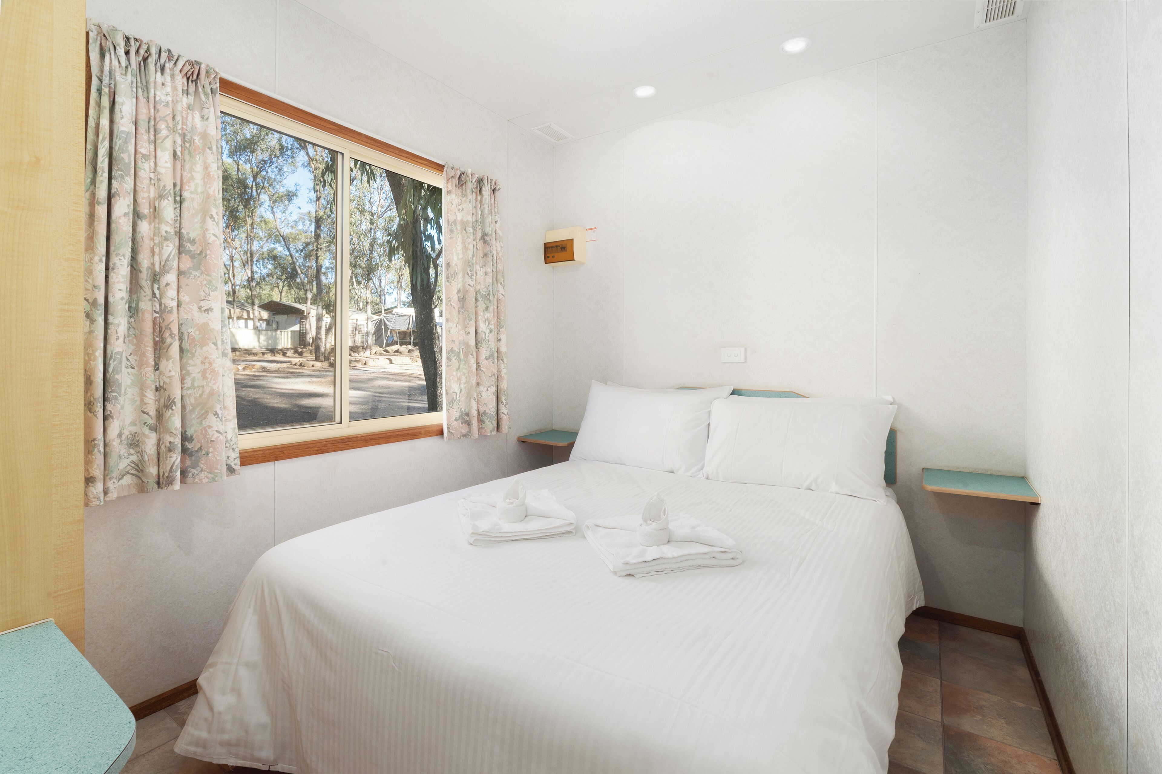 A bedroom with a large bed, a window with curtains, a bedside table, and a view of trees outside.