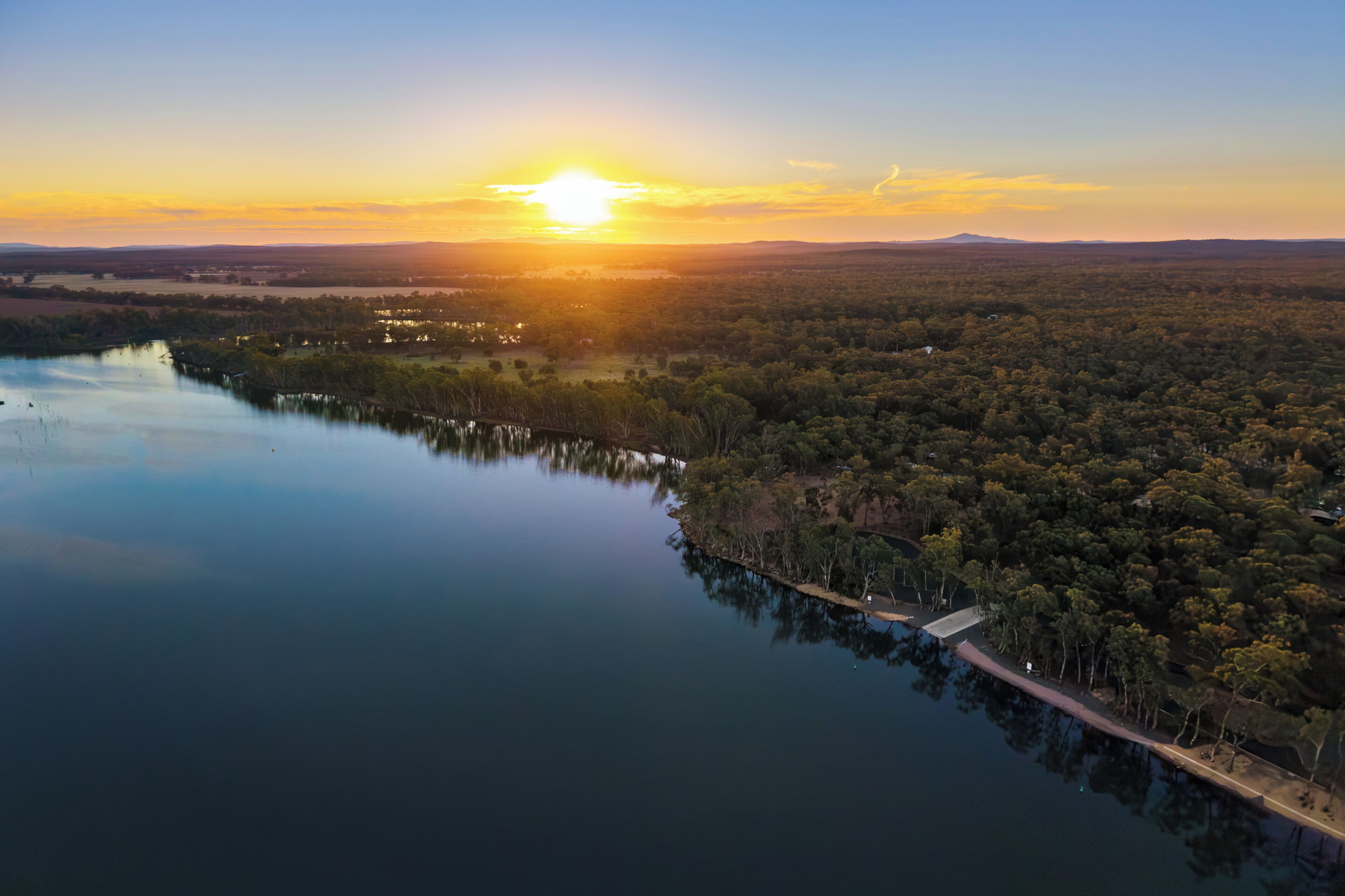 A serene lakeside view with a sunset, calm water, and dense forest.