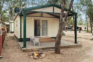 Ein kleines, eingeschossiges Mobilheim mit überdachter Veranda, Feuerstelle und Satellitenschüssel.
