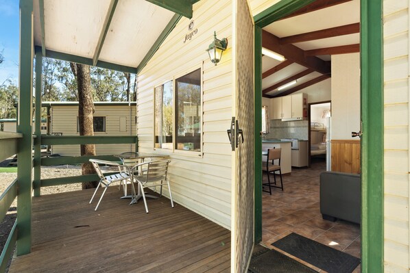 A covered outdoor area with a wooden deck, metal chairs, and a table. - Tiny Away Stay – Laanecoorie Lakeside (Laanecoorie)