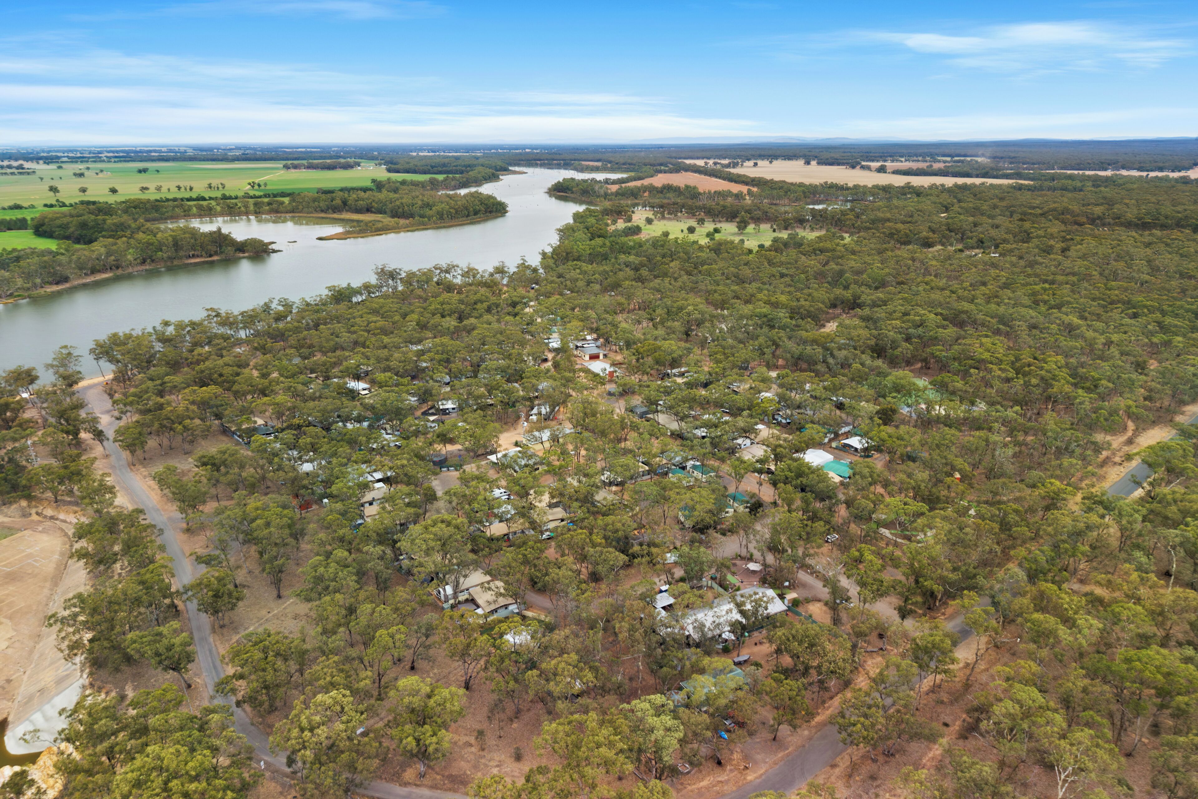 Vista aérea de una zona rural con un río, casas dispersas y vegetación densa.