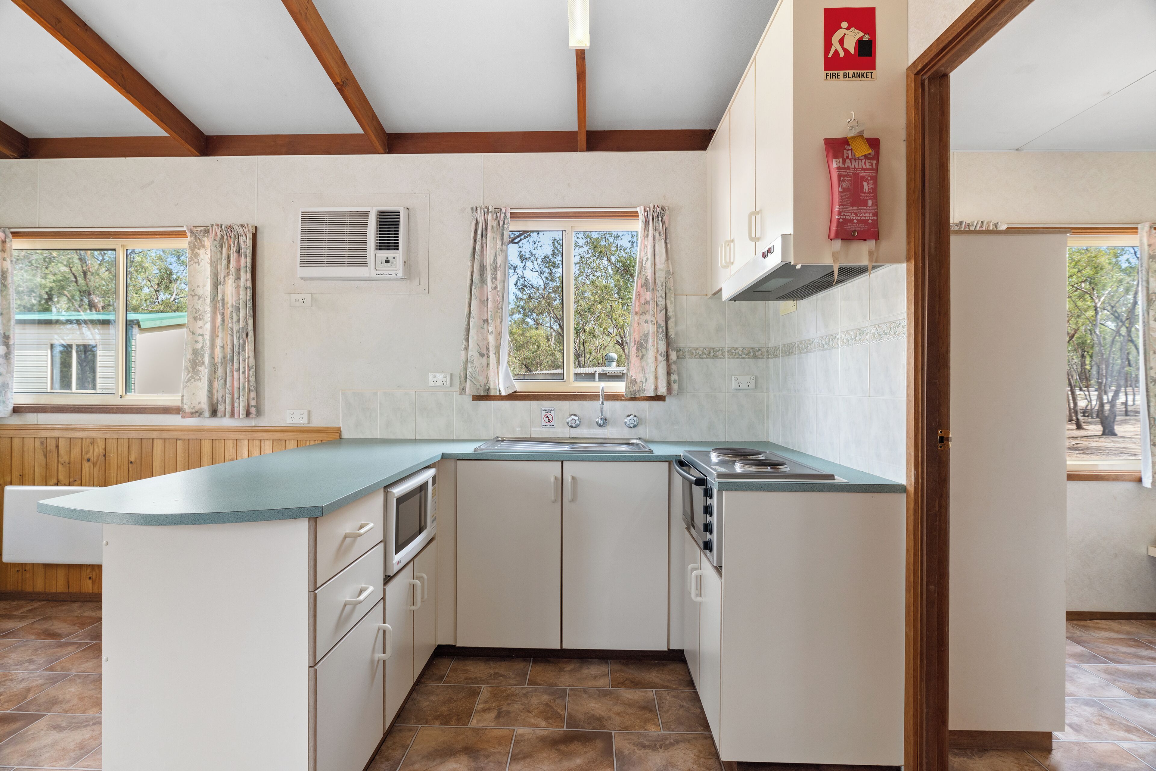 Una cocina con isla integrada, muebles blancos, un ventanal con cortinas y señal de manta ignífuga.