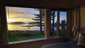 A bedroom with a large window offering a view of a lake and forest. - Mid-coast Dream- Beautiful Oceanfront home with spectacular views! (St. George)