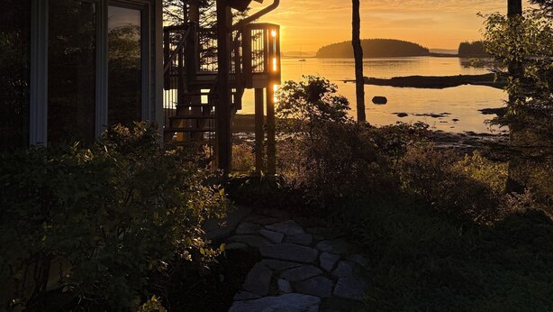 A wooden deck with a stone pathway leading to a house overlooking a body of water with distant landforms. - Mid-coast Dream- Beautiful Oceanfront home with spectacular views! (St. George)