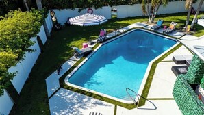 A rectangular swimming pool with a tiled deck, surrounded by lounge chairs and umbrellas.