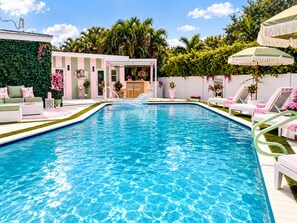 A swimming pool with lounge chairs and a bar area, surrounded by greenery and a white fence. - Party villa. Steps to Beach. Cruise port. Pier 66 (Fort Lauderdale)