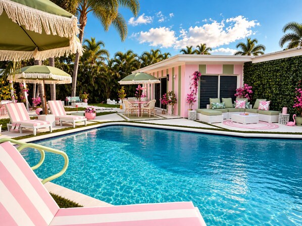 A pool area with lounge chairs, a table, and umbrellas.