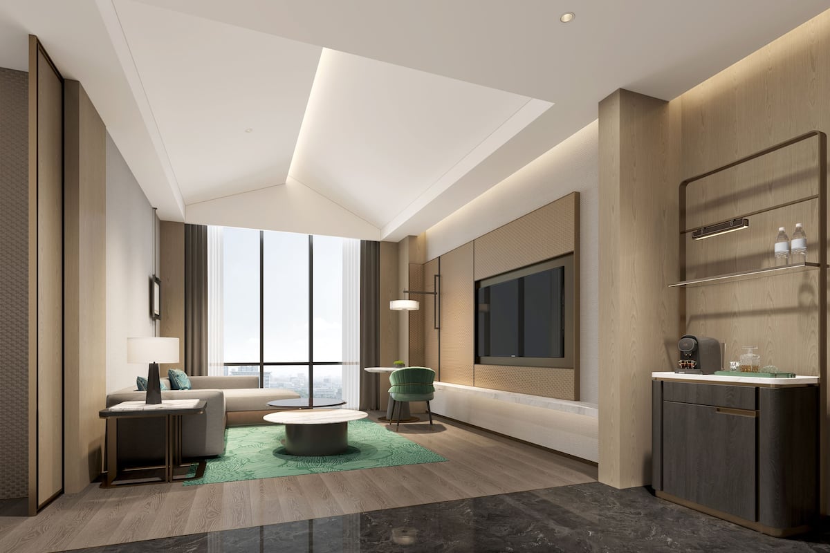 A modern hotel room with a large TV, a sofa, a coffee machine, and a small table.
