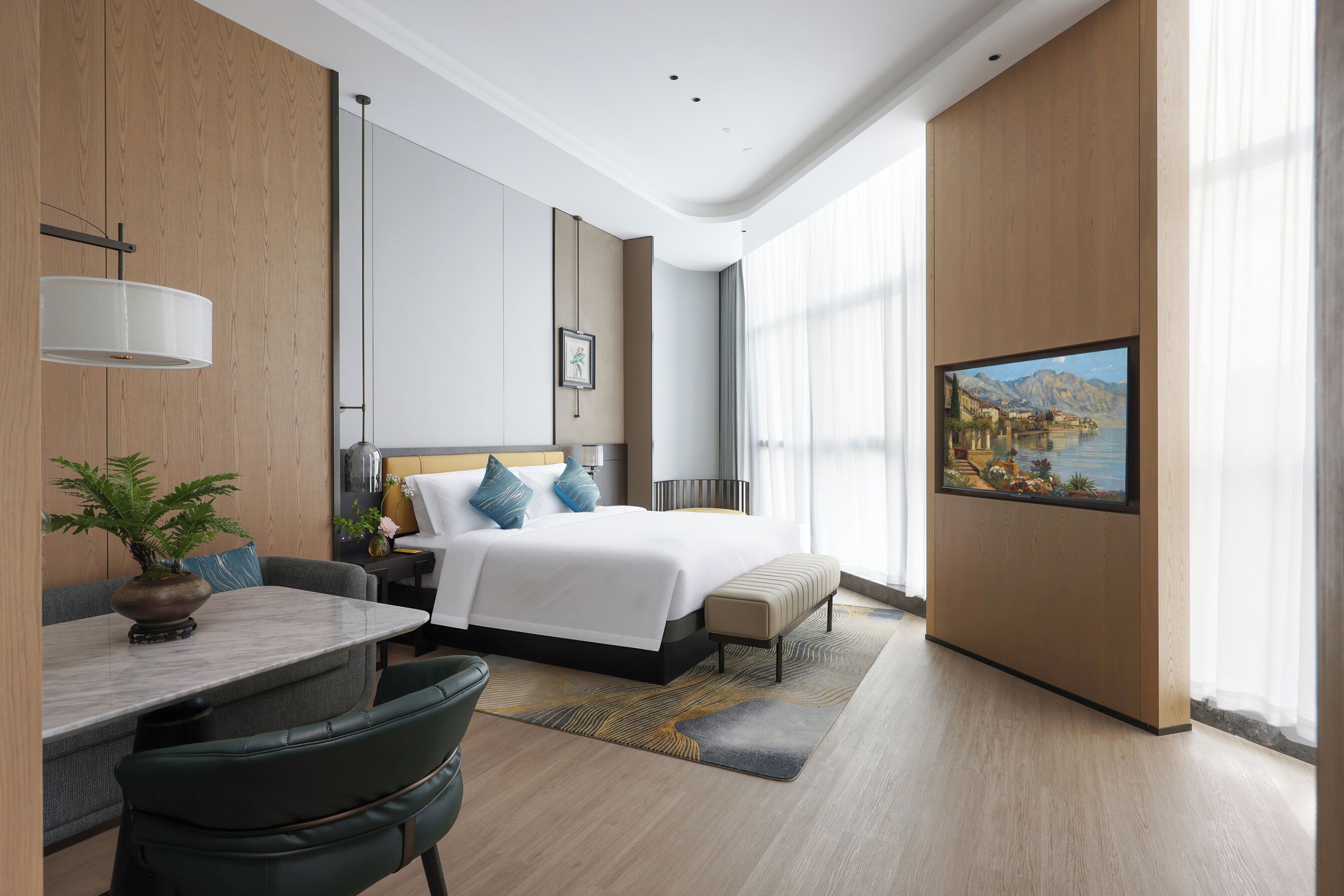 A modern hotel room with a bed, bedside table, lamp, and a painting of a landscape.