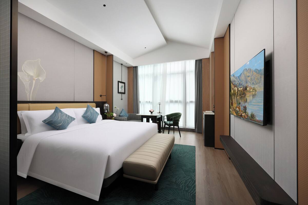 A modern hotel room with a large bed, a desk, a chair, and a television on the wall.