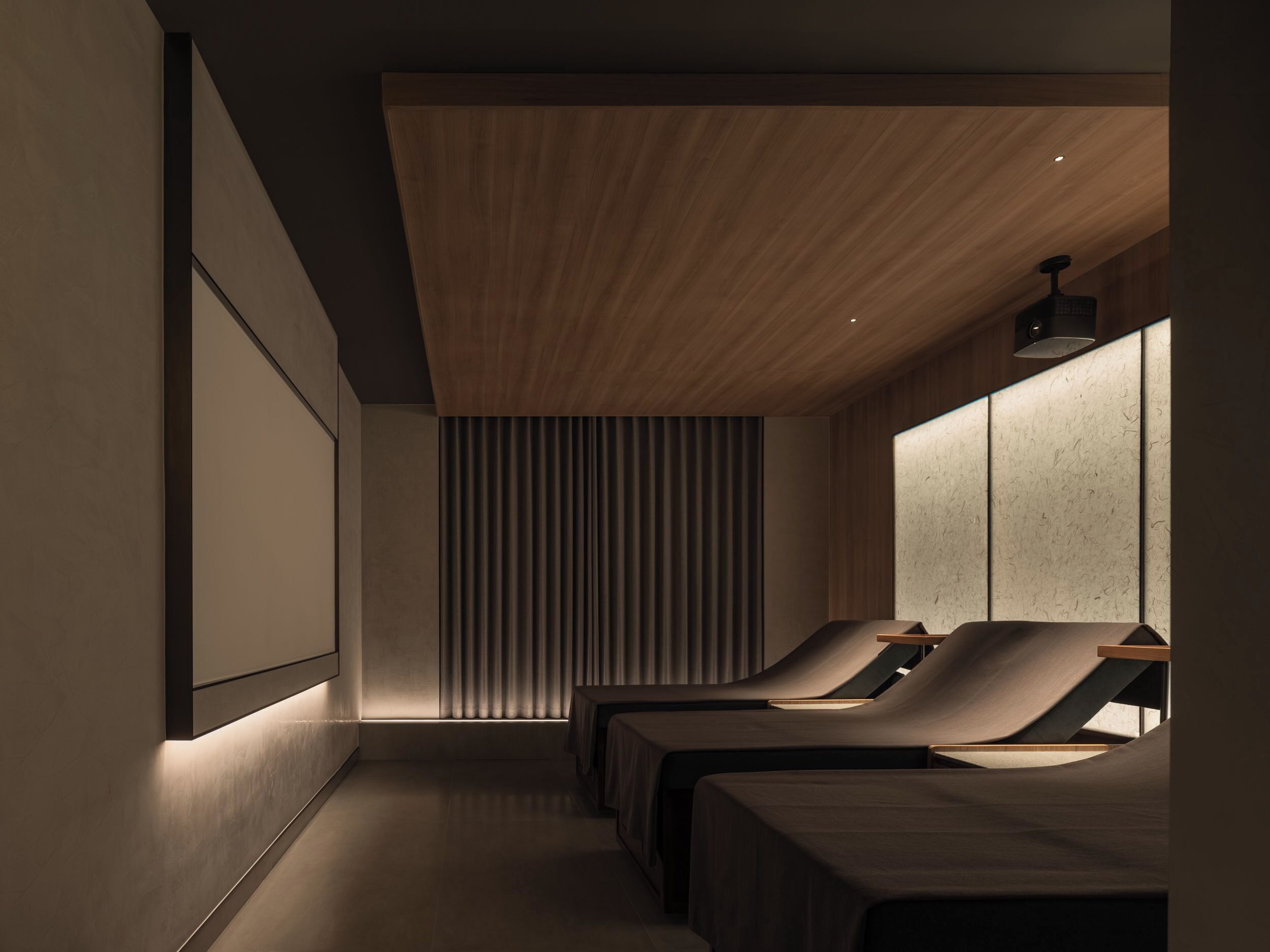 A modern spa room with two massage tables, a wooden ceiling, and a large window with blinds.