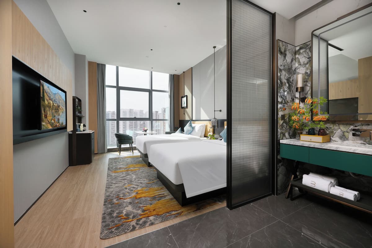 A modern hotel room with a large bed, a separate bathroom, a city view, and a flat-screen TV.