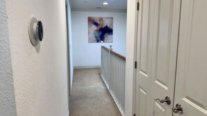 Ein Flur mit Teppichboden, einer weißen Wand, einer Tür mit Griff und einer Deckenleuchte.