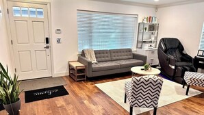 Ein Wohnzimmer mit einem grauen Sofa, einem schwarzen Ledersessel, einem kleinen runden Tisch und einem Bücherregal.