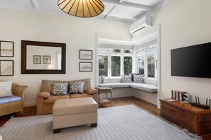 A living room with a sofa, a wooden side table, a large window seat, and a flat-screen TV. - Perfect Mt Eden Bungalow (by Furnished Rentals) (Auckland City)